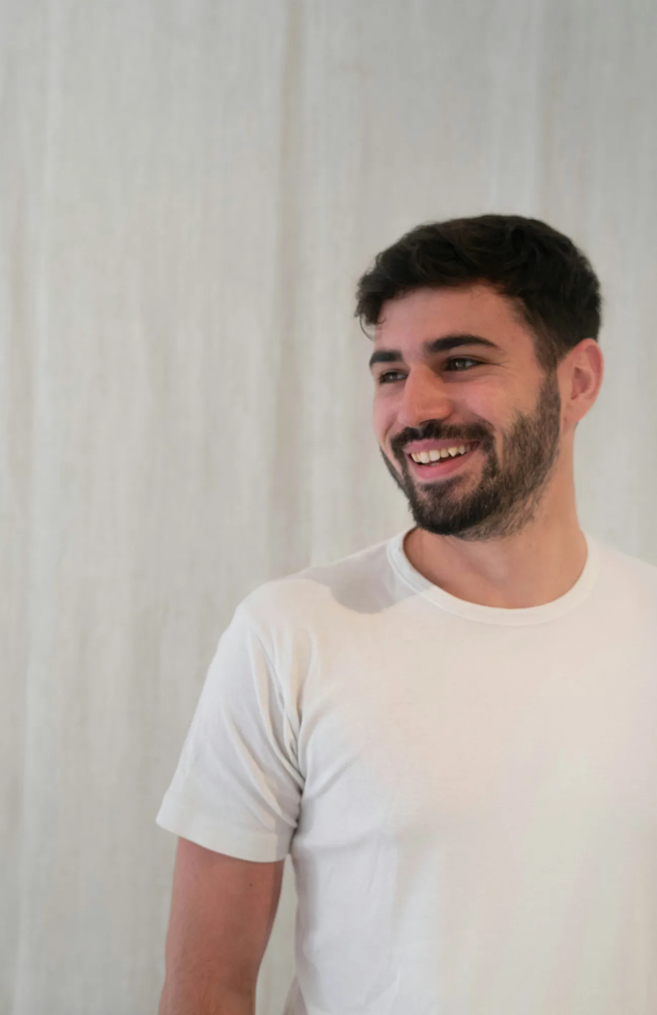 A young man in a white T-shirt smiling warmly